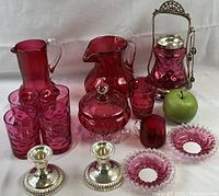Full lot arrangement showing all cranberry glass pieces and 2 sterling silver candle holders with green apple for scale