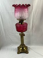 Full view of cranberry antique oil lamp showing brass base, cranberry glass font, and etched shade.