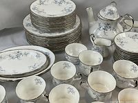 Stacked plates at left with two stacks of plates and cups beside teapot at right