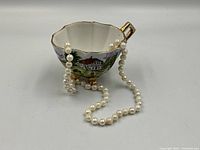 Pearl necklace draped over teacup showing overall appearance of both items