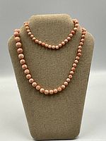 Single necklace displayed on bust stand, showing the uniform pink coral beads and knotted string.
