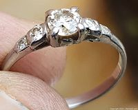 Ring held between thumb and forefinger showing central diamond and shoulder stones