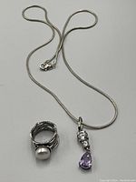 Sterling silver ring with white pearl and silver snake chain necklace with pendant displayed on white background