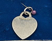 Close-up of the sterling silver heart-shaped pendant showing the Tiffany & Co. 925 hallmark and attached purple bead.