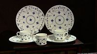 4 dinner plates and 3 cups with blue floral designs on white porcelain marked Churchill England, displayed on a dark surface.