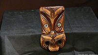 Front view of the carved wooden Maori Koruru mask showing detailed carving and abalone eyes.