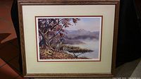 Framed watercolor painting showing the full scene with deer, tree, water, and distant foggy mountains.