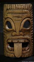 Front view of the wooden tiki mask showing carved facial features and tongue.