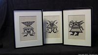 Front view of three framed prints of African art images, showing black abstract figures on beige backgrounds in black frames with white mats.