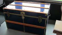 Front side of blue traveling trunk showing wood banding, brass hardware, and leather handles.