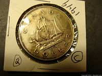Front of 1949 Canadian Silver Dollar showing Bluenose sailing ship, coin encased in protective flip with handwritten date and markings.