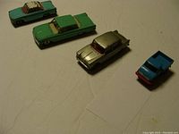Four diecast toy cars: two light green, one light blue with paint wear, one silver, and one small blue truck.