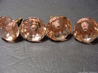Four pink crystal glass drawer pulls laid on black fabric, showing front and side views, highlighting faceted design and pink tint.
