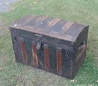 Front view of dome top steamer trunk showing tin clad, wooden slats, metal lock and hooks