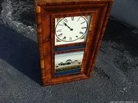 Full view photo of the antique ogee clock showing wooden tiger maple veneer case, dial, and painted glass panel.