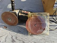 Side view of black Craftsman grinder with sanding disc attached and two additional sanding discs in packaging next to it.