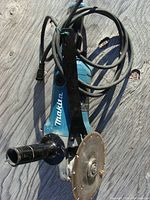 Full view of the Makita GA70 angle grinder showing the blue body, attached metal handle, power cord and 7-inch diamond cutting blade.