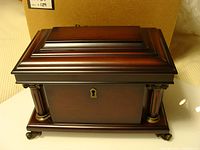 Closed view of the jewelry box showing dark wood finish, decorative columns, and brass accents.