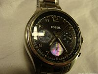 Front view of Fossil chronograph wristwatch showing black dial, gold-tone numerals, and iridescent sub dials.