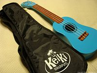 Full view of the blue Keiki ukulele showing body and attached black soft carry case with Keiki logo.