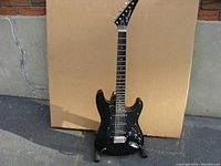 Full view of the black Kingston electric guitar on stand showing body shape and hardware.