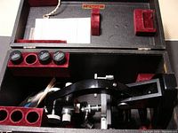 Top view of microscope inside original black box with red velvet inserts holding several eyepiece lenses and accompanying paperwork.