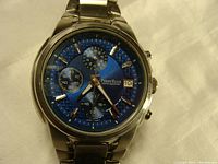 Close-up photo of the blue dial Perry Ellis chronograph watch showing the three subdials, date window, and push button clasp on the band.