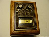 Front view of wooden post office lock box, showing two rotary letter dials, latch, symbolic eagle, and number window 1216.