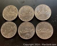 Six Canadian Voyager one dollar coins arranged on a black surface, showing the reverse design and year dates clearly.