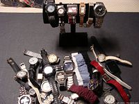 Full view of all watches including those on display stand and scattered on surface, showing diverse styles and bands.
