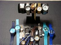 Overview of all fourteen watches displayed on a black cylindrical holder and flat surface.