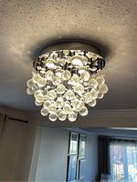 Chandelier ceiling fixture lit, showing round brass base and multiple hanging clear glass or crystal round droplets suspended from it.
