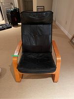 Front view of wooden armchair with black cushioned seat and back showing wear and creasing.