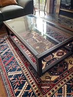 Full view of wood framed coffee table with clear glass top on patterned rug.