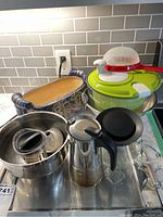 Kitchen items including salad spinner, carafes, colander, ceramic dish, and skimmer spoon arranged on countertop