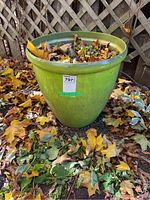 Single green outdoor planter with dirt and dry leaves inside, situated on a ground with fallen leaves.
