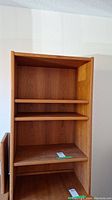 Front view of the three-shelf wooden shelving unit showing the shelves and back panel in medium brown finish.