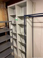White wood multi-shelf shelving unit showing multiple shelves and a solid back panel, placed in a basement storage area with other shelving units nearby.
