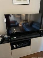 Front view of 48-inch TV on stand with living room reflection, tag on left bezel