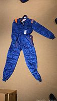 Full view of blue Sparco racing suit laid flat showing overall quilted design and elastic cuffs.