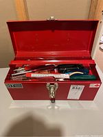 Closed red Stanley metal toolbox with some hand tools visible inside.