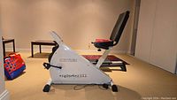 Side view of the white Kettler SX1 stationary bike showing the frame, seat with backrest, pedals, and exercise bands attached at the front.
