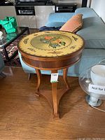 Full side view of the round wood side table with butterfly and flower painted top near blue sofa.