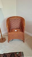 Front view of vintage wicker chair showing curved wicker back with fabric cushion, seat and legs. Light brown cushion with floral pattern.