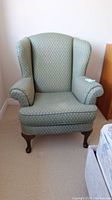 Front view of green fabric wingback chair with patterned upholstery and wooden cabriole legs.