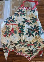 Apron with cardinal and holly print showing front with pocket and straps, laid flat on table