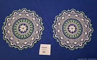 Two round hand crocheted doilies with green and white pattern on a blue background.