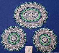 Photo of one oval and two round hand crocheted green and white doilies on blue background with size card.