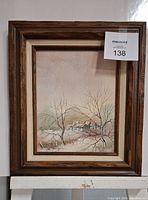 Framed winter scene painting with wooden frame, showing the snowy landscape and houses.