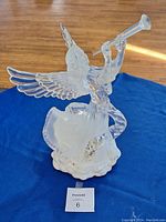 Clear glass angel figurine on a blue cloth background, detailing wings and trumpet, base visible.